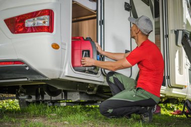 40 'lı yaşlarındaki beyaz adamlar, karavanın arka tarafındaki karavan deposundan taşınabilir gaz jeneratörünü çıkarıyorlar. Kuru Kamp Elektrik Üreticisi.