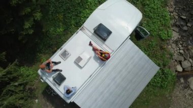 Caucasian Family Chilling Out on a Top of Their Camper Van Motorhome Enjoying Summer Vacation Sun. Rving Theme. 