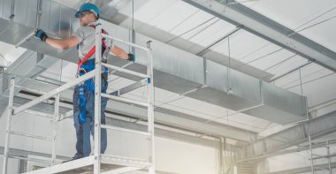 Alüminyum İskeledeki Profesyonel HVAC İşçisi Yeni Yapılmış Ticari Yapı Deposunun içine Hava Kanalı Kuruyor. Endüstriyel Tema.