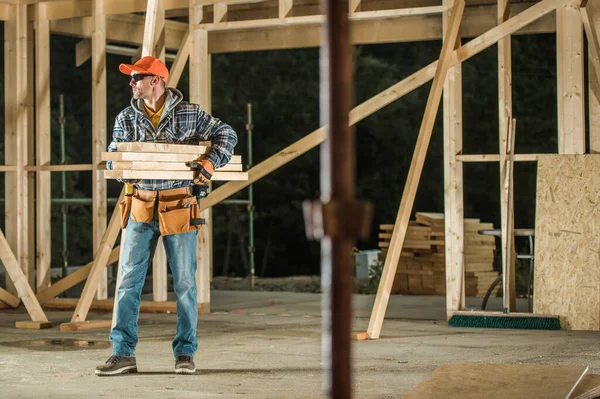 Caucasian Professional Construction Worker Moving Pieces of Wood Inside Wooden Skeleton Frame of a House. Construction Industry Theme.