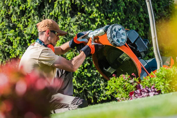 Caucasian Garden Worker in Special Gardening Wear and Safety Glasses Checking the Condition of His Grass Cutting Equipment Before Starting to Mow the Lawn.