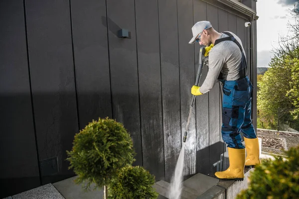 40代の男性白人家庭のオーナーが作業服を着て家の壁や近くのコンクリートのスラブを圧力洗浄機で洗うことで庭をきれいにする — ストック写真