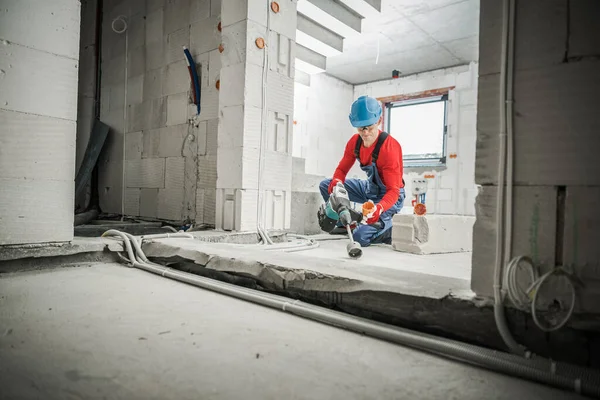 Güvenlik Miğferli Beyaz İnşaat İşçisi ve Gözlüklü Delik Testere Bıçak Eklentisini Güç Matkabıyla Kullanarak İşini Yapıyor. İnşaat alanı arka planı. Gayrimenkul Geliştirme Teması.