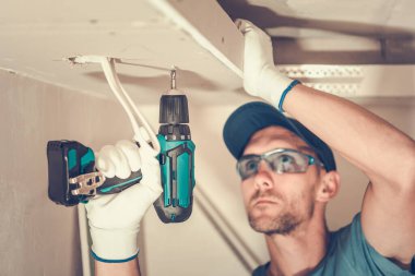 Closeup of Caucasian Contractor in His 40s Focused on Installation of the Gypsum Plasterboard Using Electric Screwdriver. Construction Site Industrial Theme.