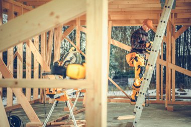 Caucasian Worker Going Up the Stepladder to Check the Roof Section of Wooden Skeleton of the Residential House Under Construction.