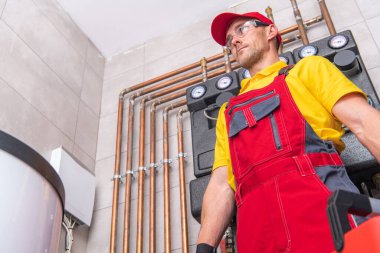 Caucasian Plumber in His Work Uniform Standing in the Middle of Technical Boiling Room Ready to Check and Repair the Piping System. Sanitary Engineering Theme.