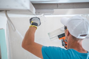 Rear View of Caucasian Worker Filling the Wall with Gypsum Putty During Renovation Work in Newly Built Apartment. Industrial Theme.