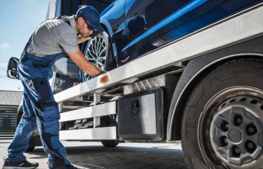 Towing Worker Delivering Brand New Car from Dealer to Client. Caucasian Man Checking the Fastenings to Ensure Safe Transportation on His Tow Truck.