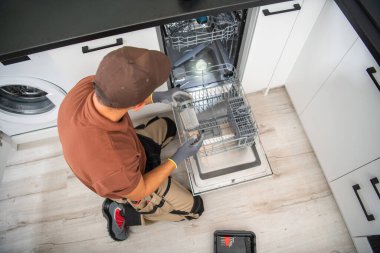Installer Assembling and Preparing For Use a Freshly Installed Dishwasher in a Renovated Modern Kitchen. Professional Household Services. Kitchen Equipment Theme.