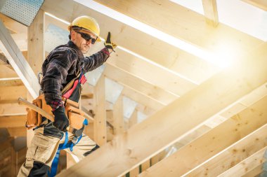 Fully Equipped Professional Construction Worker Securing Wooden Planks in the Roof Section Skeleton of New Residential House Hammering Nails With a Hammer.