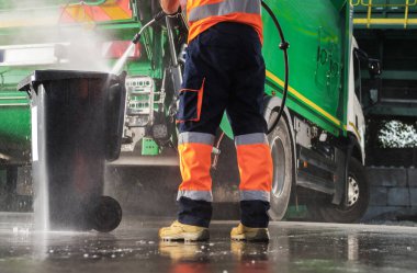 Caucasian Garbage Truck Operator Pressure Washing Black Trash Can After Waste Collection. Junk Truck Built In Washer Using.
