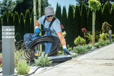 Professional Landscaping Worker in His 40s Preparing Irrigation Plastic Pipe For a Trickle System. Gardening Industry Theme.