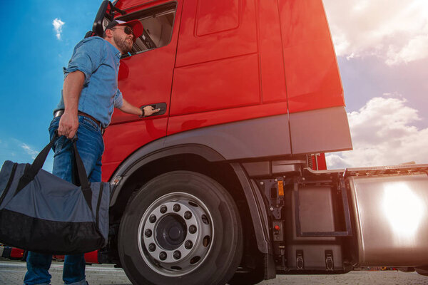 Caucasian Lorry Driver With a Bag in His Hand Opening the Cab Door to His Red Semi Truck Ready to Start Another Route and Complete a Delivery. Heavy Duty Transportation Theme.