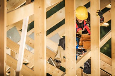 Fully Equipped Builder Working with Wooden Planks in Roof Section of Canadian Style Residential Building Under Construction. Industrial Theme.