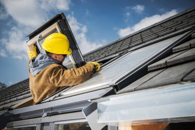 Caucasian Middle Aged Man in Yellow Hard Hat Checking and Fixing the Roof Window in Residential House. Professional Home Repair Services Theme.