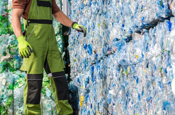 Caucasian Waste Management Worker in Front of a Pile of Pressed Plastic PET Bottles. Trash Sorting Facility.