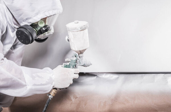 Automotive Industry Painter Worker Wearing Breathing Safety Mask and Uniform Painting Vehicle Body with a White Paint. Transportation Theme.