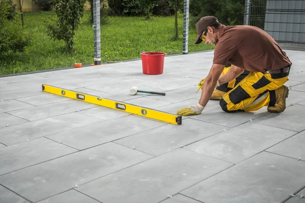 Caucasian Construction Worker Building Modern Patio Concrete Tiles Floor in a Residential Backyard.