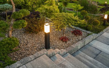 Professionally Landscaped Backyard Garden Illuminated with Outdoor Bollard Lamps Installed Along the Path in the Tree Bark Mulch.