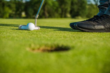 Closeup of Golfer Standing on a Golf Course Holding Putter in Position Behind the Ball Near the Cup Ready to Finish the Play with Hole Out.