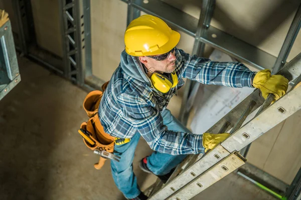 在建筑工地拍摄的黄帽专业承建商爬上梯子的头像 使用中的建筑工具及设备 — 图库照片