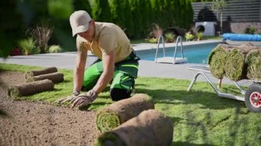 Residential Landscaping Theme. Professional Caucasian Landscaper Installing New Grass Turfs in the Backyard Garden.