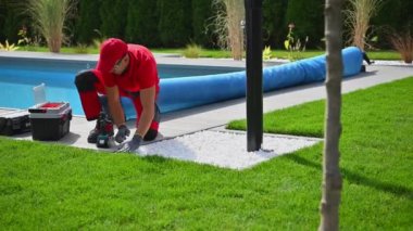 Beyaz adam arka bahçesindeki havuz güvertesinde birleşik yüzme havuzu yapıyor. Matkap Sürücüsü Kapat.