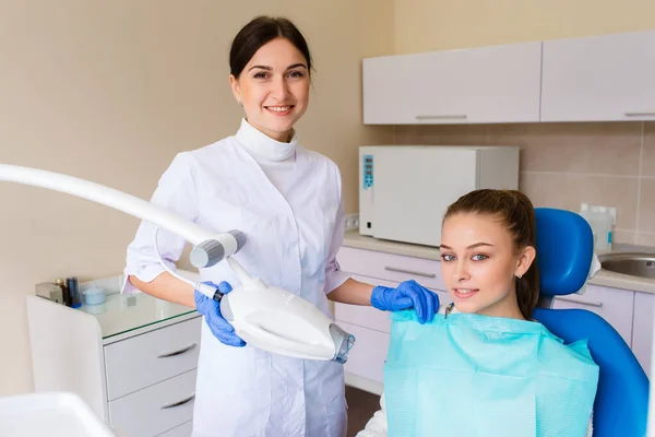 特別な服を着た若い専門医の歯医者の女性は女性患者の歯の色のパレットを示しています 歯のホワイトニングコンセプト — ストック写真