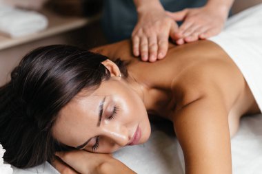 Güzellik salonunda sırt masajı yaparken gözleri kapalı uzanan genç bir kadın. Müşterisiyle çalışan profesyonel bir masöz. Güzel kız spa merkezinde masaj yaptırıyor.