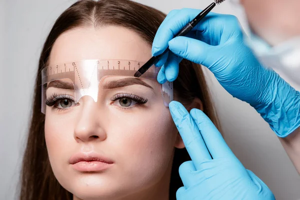 Microblading eyebrows work flow in a beauty salon. Woman having her eye brows tinted. Semi-permanent makeup for eyebrows. Focus on model\'s face and eyebrow