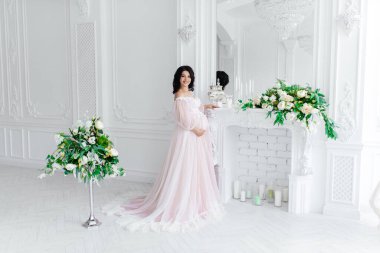 Aydınlık bir odada elbise giymiş hamile güzel bir kız.