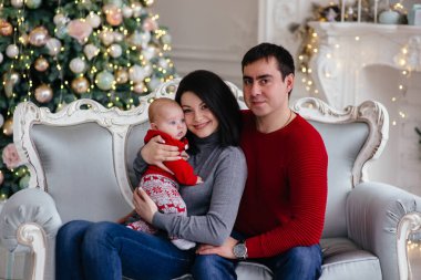 Mutlu bir aile Noel ağacının yanındaki kanepede oturur..