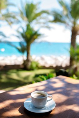 Sabah balkonda beyaz kahve fincanı, güneş ışığı ve deniz manzaralı. Sabahları serinlemek için sıcak kahve. Konseptte kahve zamanı..