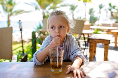 Güzel Latin kız açık hava kafeteryasında pipetle soda içiyor.