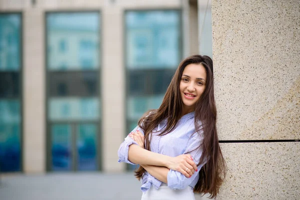 Sarı duvarın önünde duran, saçları okşayan, baskılı bluz ve kot giyen esmer kadının portresi.