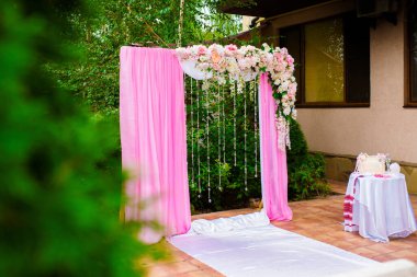 Düğün kemeri dışarıda kumaş ve çiçeklerle süslenmiş. Güzel bir düğün hazırlığı. Bahçedeki yeşil çimlerde düğün töreni. Festival dekorunun bir parçası, çiçek aranjmanı.