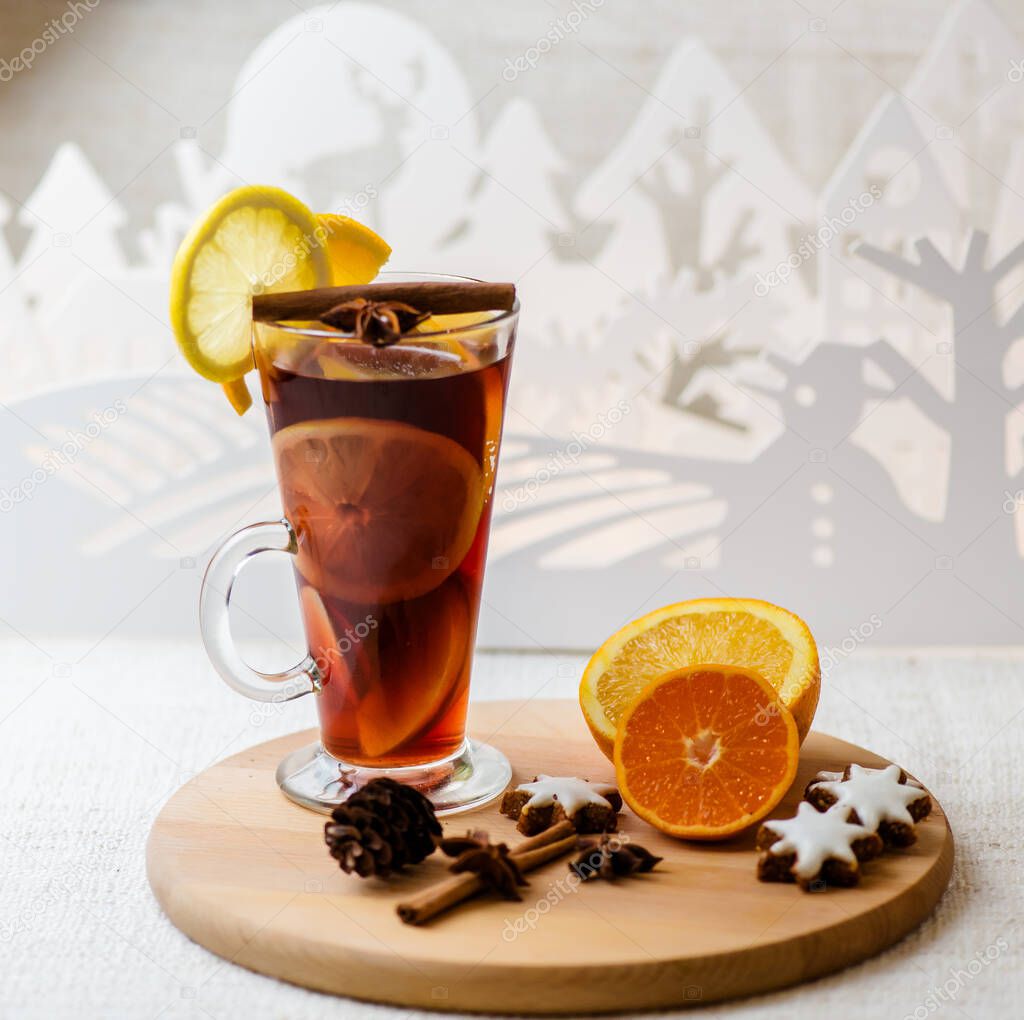 Hot mulled wine in a glass with orange slices, anise and cinnamon sticks, star cookies on vintage wood table. Christmas or winter warming drink with recipe ingredients around
