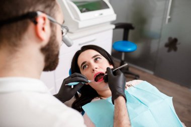 Güzel genç bayan dişçide. Dişçi koltuğunda oturuyor ve dişçi dişlerine diş teli takıyor. Estetik kendi kendine hizalanan dilsel kilitler takıyor.