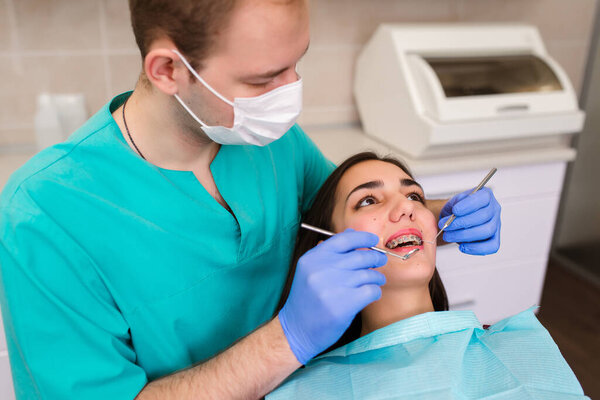 A male dentist examines a patient's teeth using a professional dental microscope. The client lies on the dentist's chair