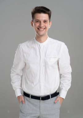 Handsome confident young man standing and smiling in a white shirt on grey background