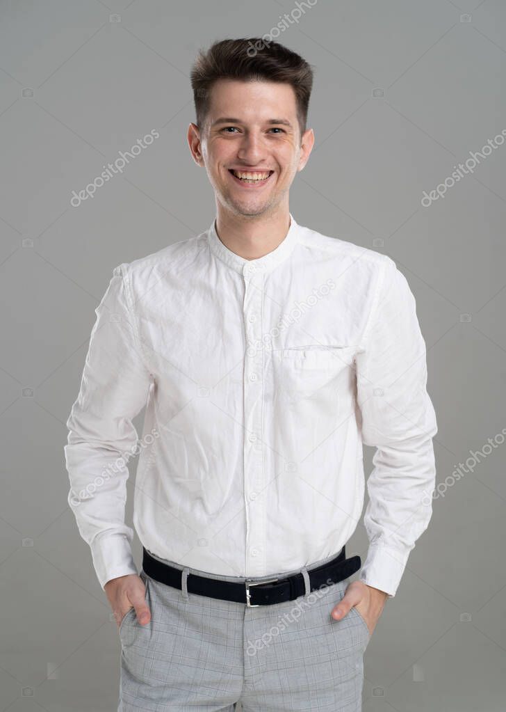 Handsome confident young man standing and smiling in a white shirt on grey background