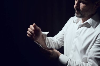 Adam kol düğmelerini siyah arka planda beyaz bir gömleğe takıyor.