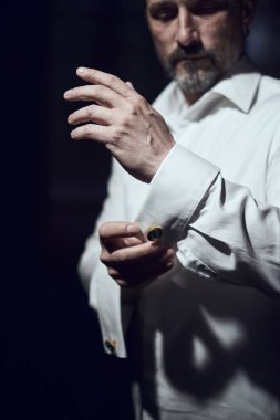 man fastens his cufflinks on sleeves on a white shirt on dark background