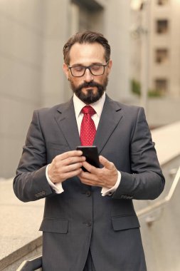 Adam binanın arka planında cep telefonu mesajları kullanıyor. Takım elbiseli beyaz sakallı adam elinde akıllı telefon tutuyor. iş çalışıyor.