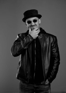 Deri ceketli, çenesini ovuşturup yüzünü buruşturan modaya uygun bir adam. Şapkalı ve gözlüklü bir adam elini cebinde tutuyor ve tereddüt ediyor.