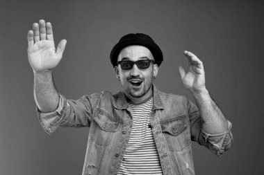 Kot ceketli çekici bir adam elleri açık, ağzı açık, şapkalı ve siyah gözlükle sallanırken heyecanlanıyor.