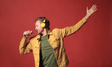 attractive handsome man in yellow jacket emotionaly singing isolated on dark red background