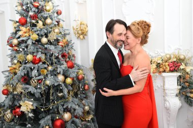 Neşeli bir adam Noel ağacının yanında dururken zevkle kadınına sarılıyor.