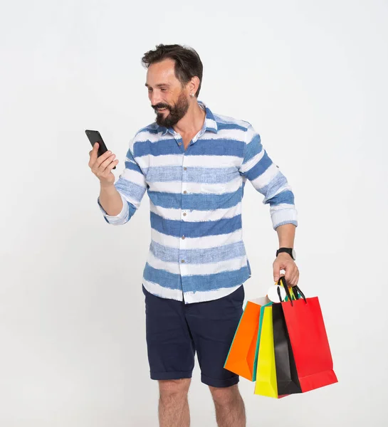 Vousatý Muž Při Pohledu Smartphone Držení Nákupních Tašek Izolovaných Bílém — Stock fotografie