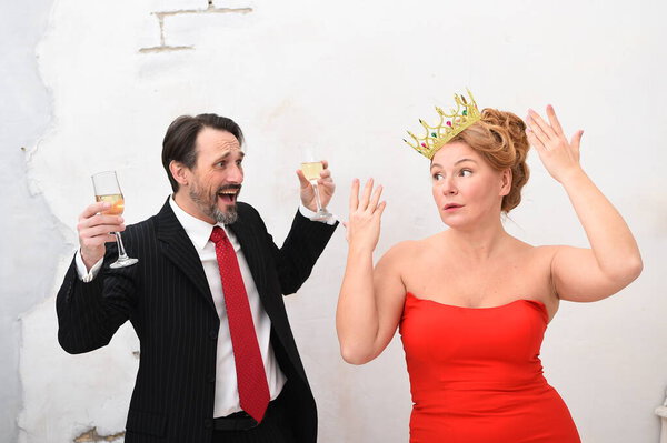Disappointed man screaming with champagne glasses in hands while his woman waving her hands and pretending nothing happened. Mature elegant couple having a conflict.